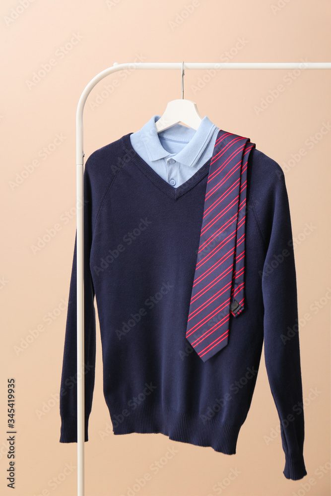 Stylish school uniform hanging on rack against color background