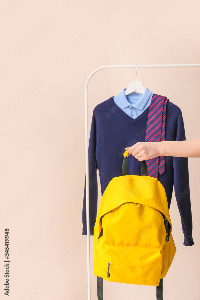 Stylish school uniform hanging on rack and female hand with backpack against color background