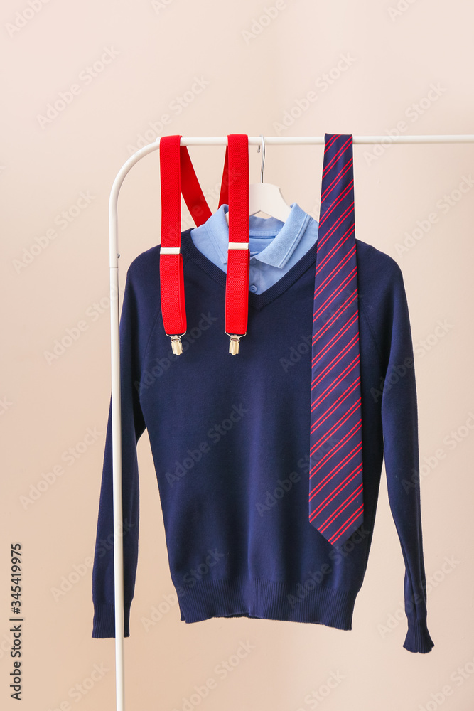 Stylish school uniform hanging on rack against color background