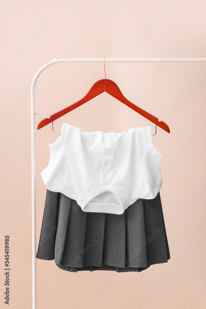 Stylish school uniform hanging on rack against color background