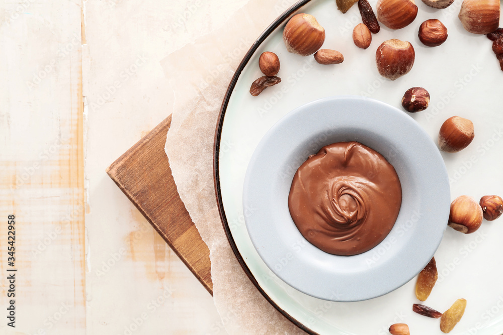 Plate with tasty chocolate paste and nuts on table