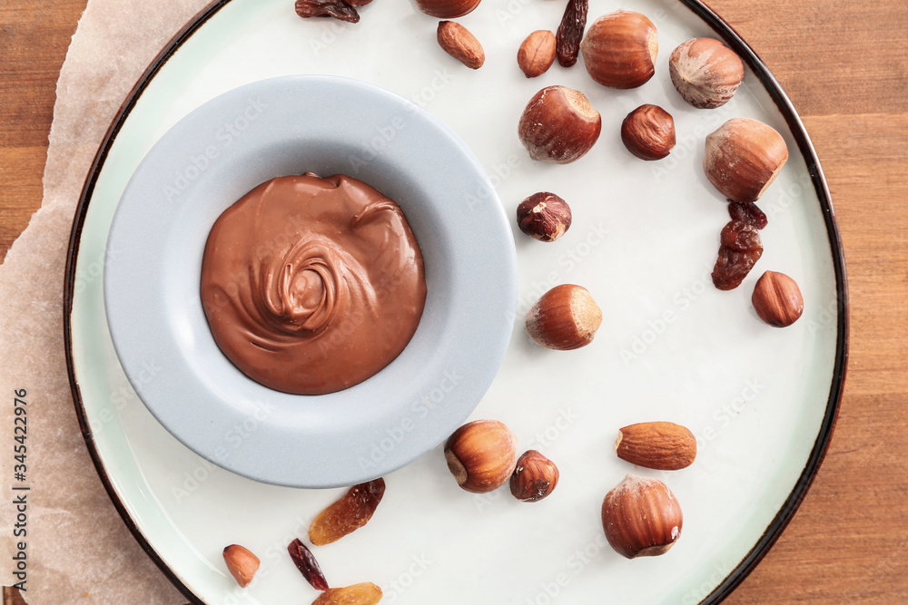 Plate with tasty chocolate paste and nuts on table