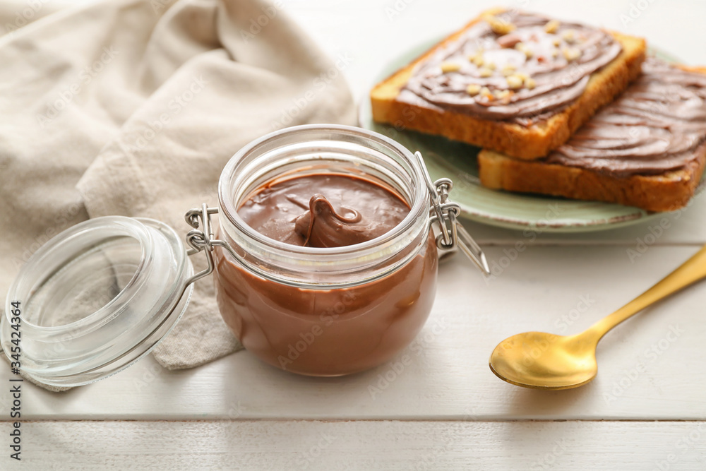 Jar with chocolate paste and bread on table