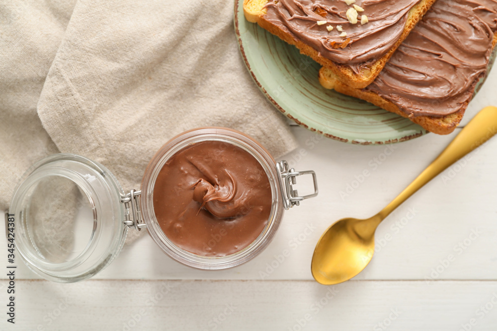 Jar with chocolate paste and bread on table