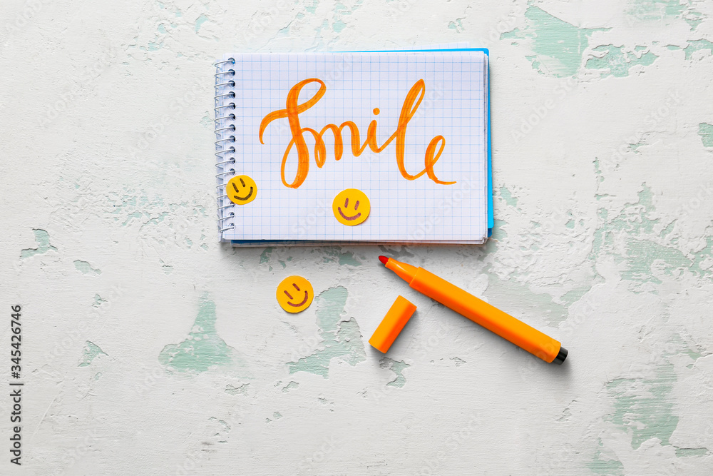 Notebook with word SMILE on light background