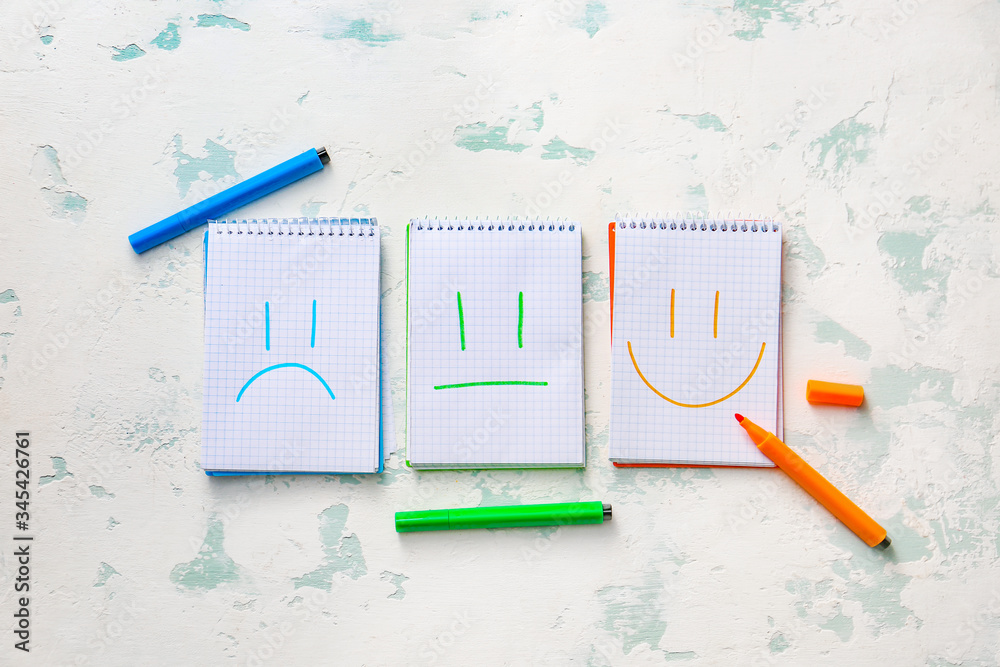 Notebooks with drawn sad, happy and neutral faces on light background