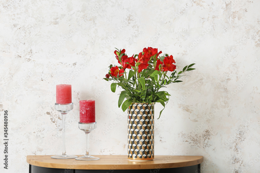 Stylish vase with beautiful bouquet and candles on table near light wall