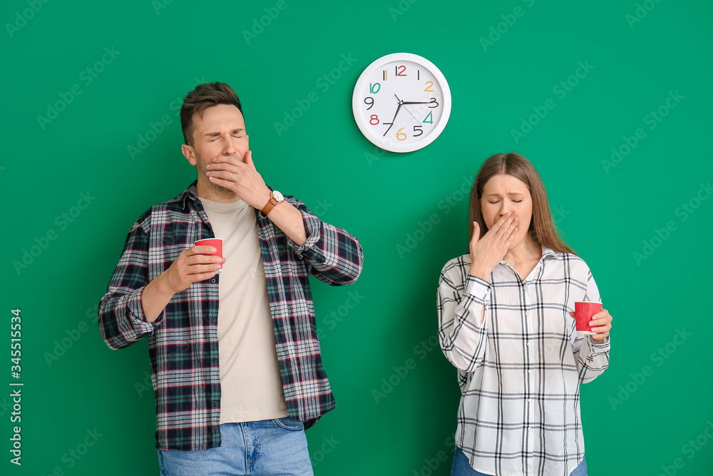 Sleepy young couple with coffee on color background