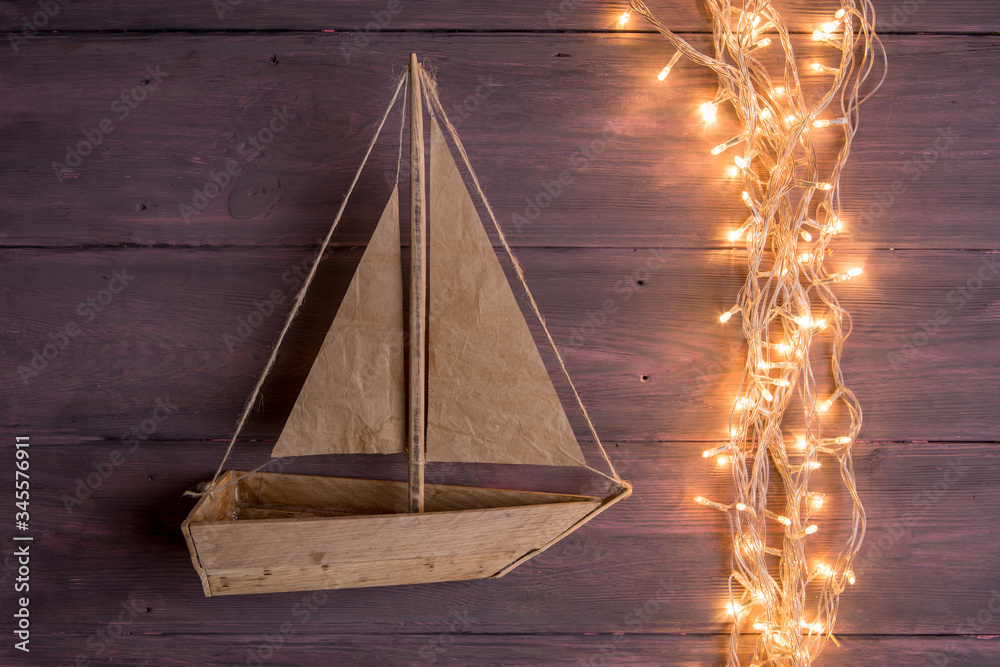 Travel and adventure creative concept - toy boat on a wooden background. Christmas lights as a sea w