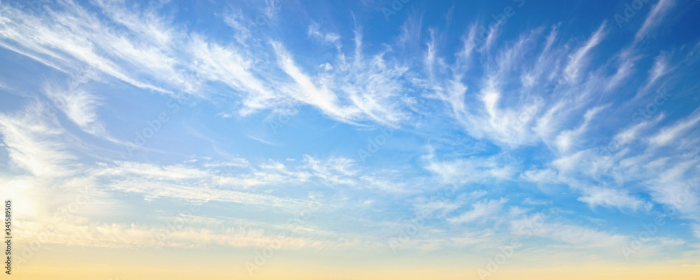 Beautiful colorful panorama of summer blue sky with white cirrus clouds during golden sunrise in sum