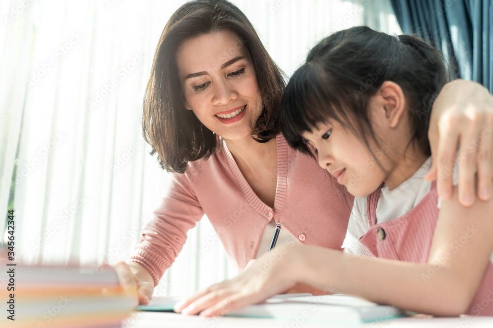 Homeschool Asian young little girl learning, reading and does homework with kind mother help, teach 