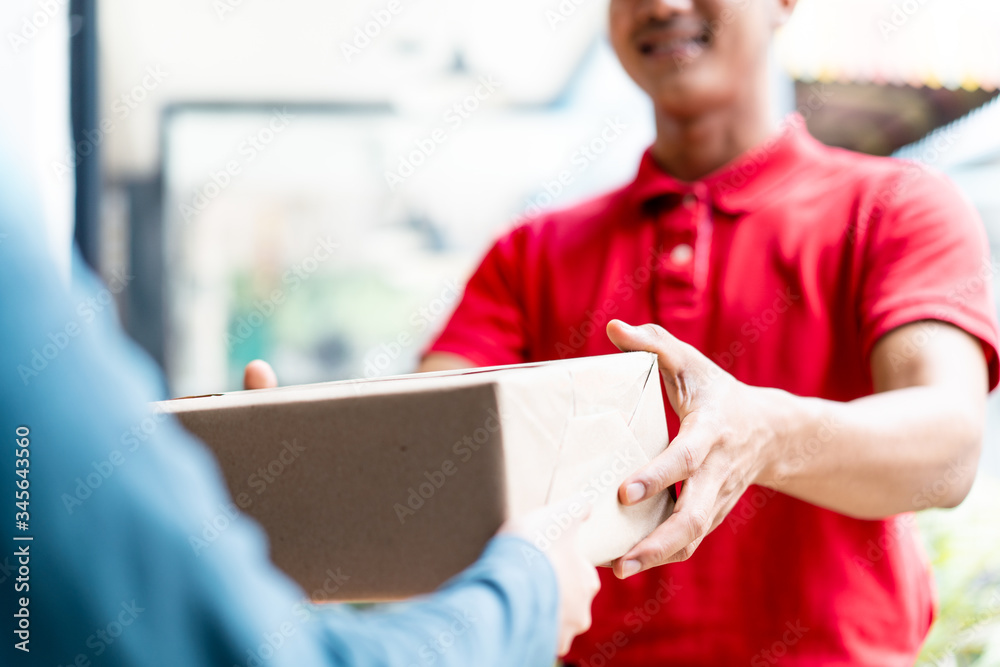 Postman delivering package of goods to home with smile and happy face. Young Asian cute girl receivi