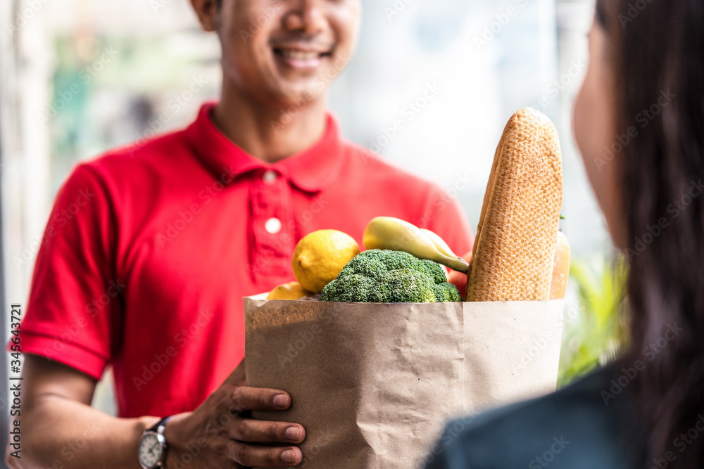 Asian deliver man worker in red color uniform handling bag of food, fruit, vegetable give to young b