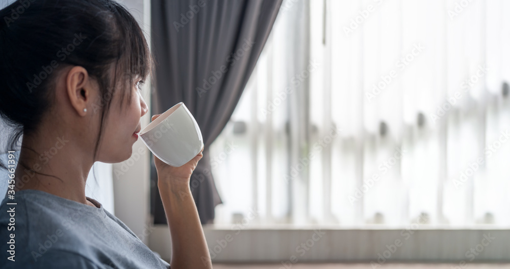 女人在卧室里手捧一杯咖啡，看着窗帘概念复古现代