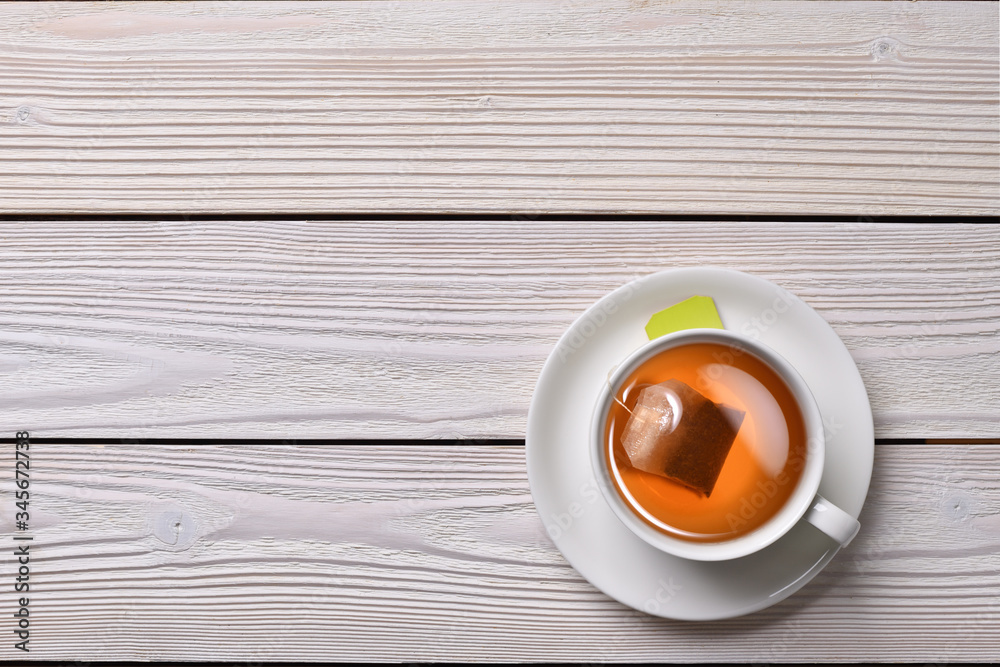 Top view of a cup of tea with tea bag on white wooden background.