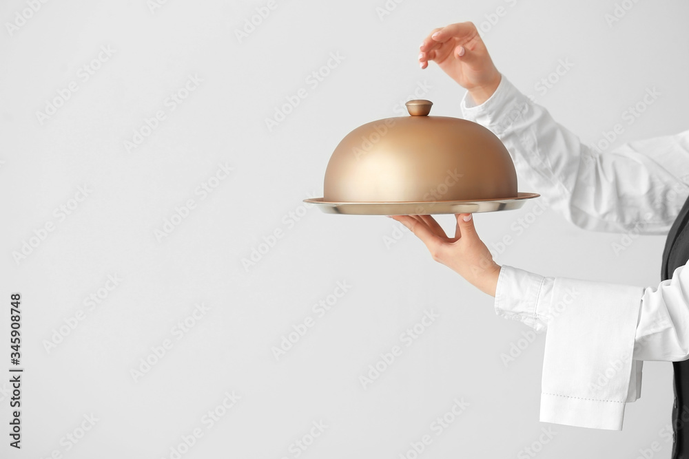 Beautiful female waiter with tray and cloche on grey background