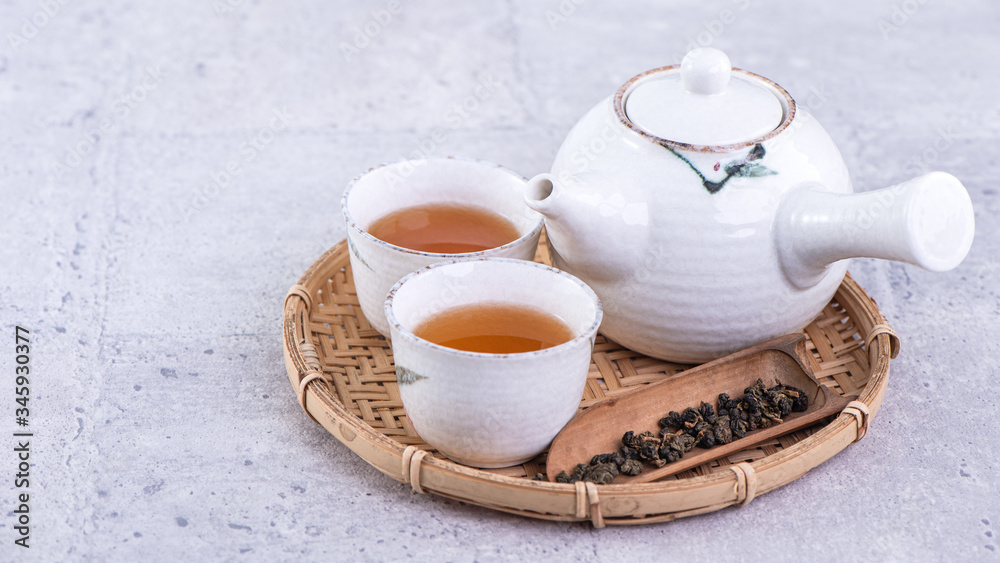 Hot tea in white teapot and cups on a sieve over bright gray cement background, closeup, copy space 