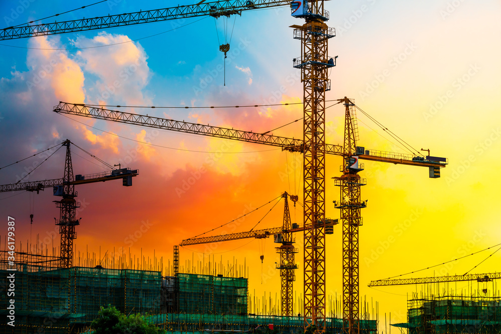 Tower crane and building construction site silhouette at sunrise.