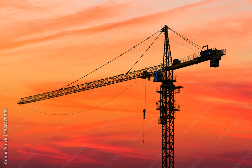 Tower crane and building construction site silhouette at sunrise.