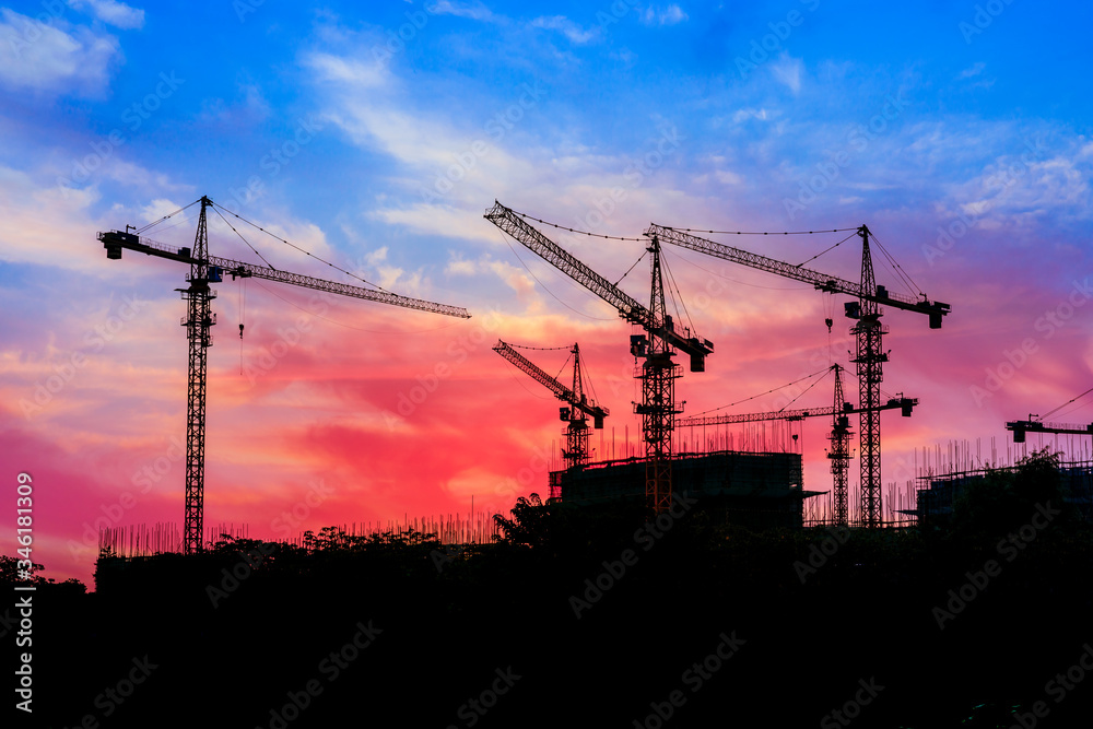 Tower crane and building construction site silhouette at sunrise.