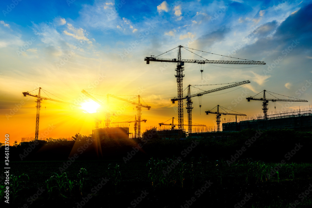 Tower crane and building construction site silhouette at sunrise.