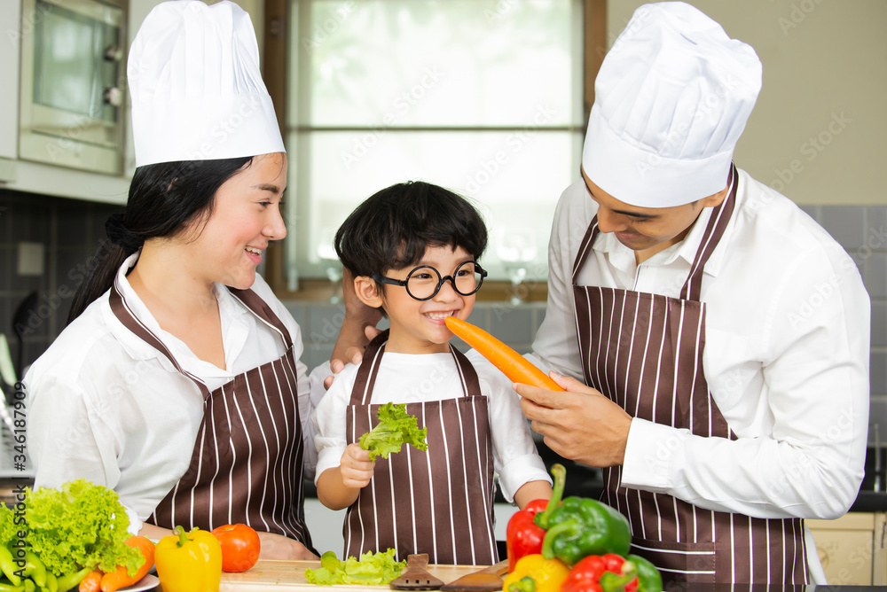 Happy cute little boy with  parents in shef hat cooking  fresh salad  vegetables  in kitchen at home