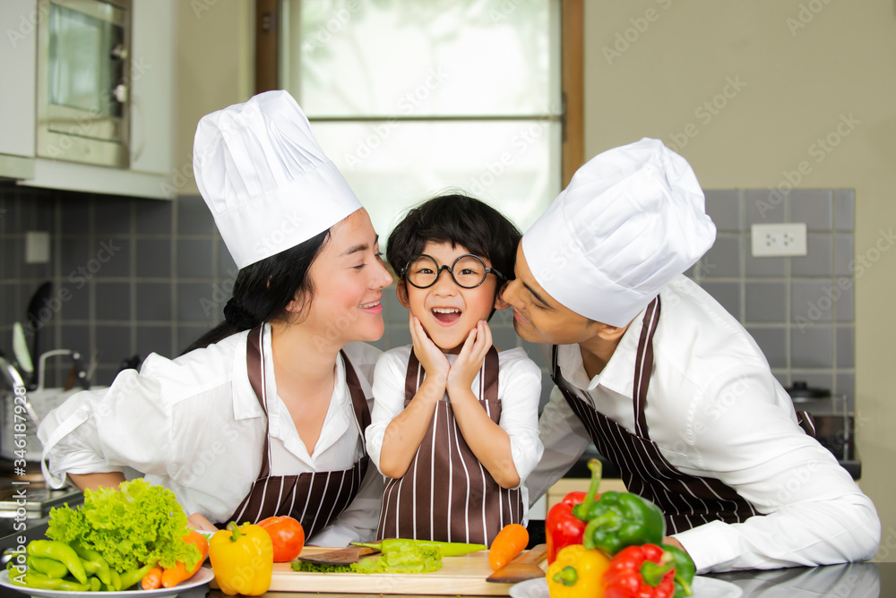 Happy cute little boy with  parents in shef hat cooking  fresh salad  vegetables  in kitchen at home