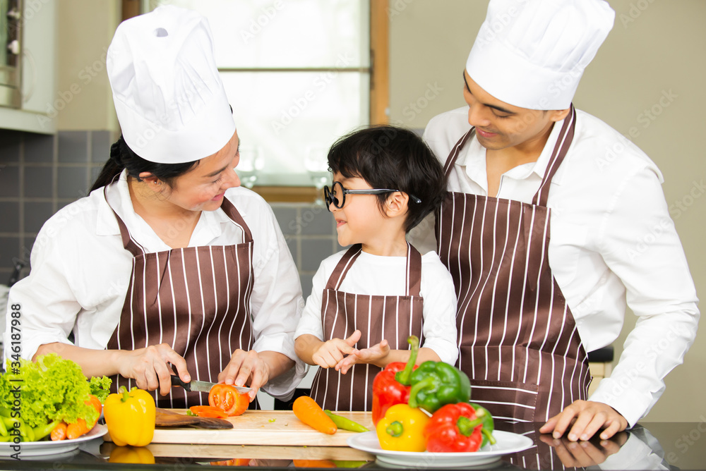 Happy cute little boy with  parents in shef hat cooking  fresh salad  vegetables  in kitchen at home