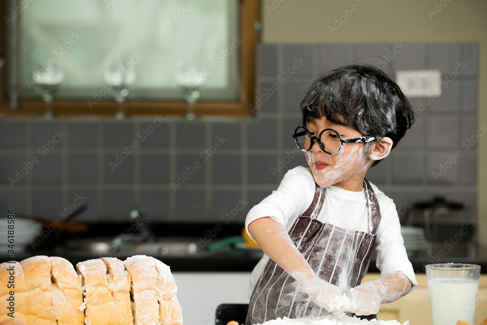 Happy cute asian  little boy in apron preparing baking the dough in kitchen room at home