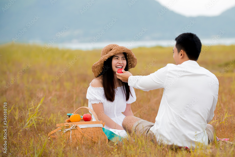 快乐的亚洲情侣在公园野餐时享用美食并弹尤克里里吉他