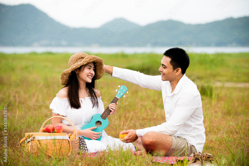 Happy asian couple enjoying  with food and playing ukulele guitar in picnic day at park