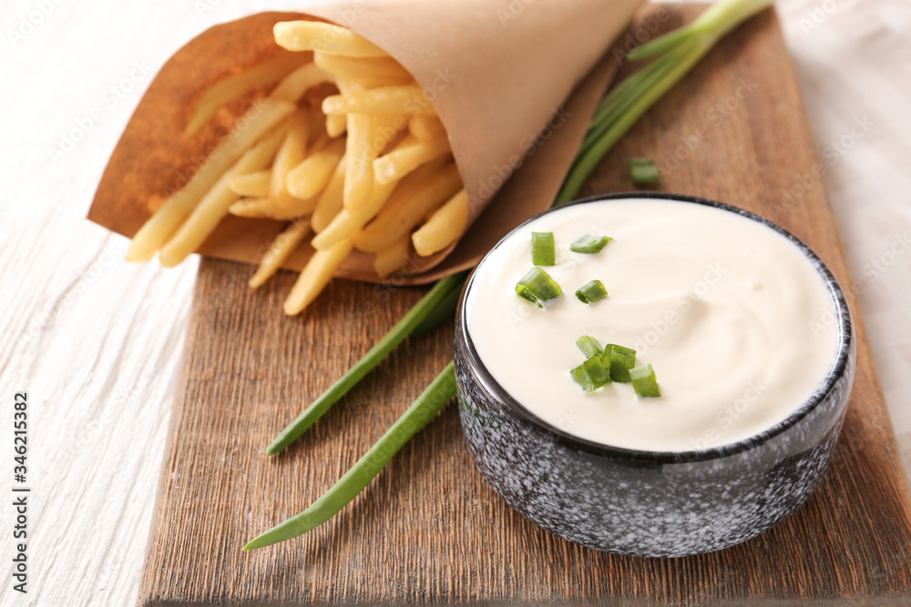 Bowl with tasty sour cream, green onion and french fries on table