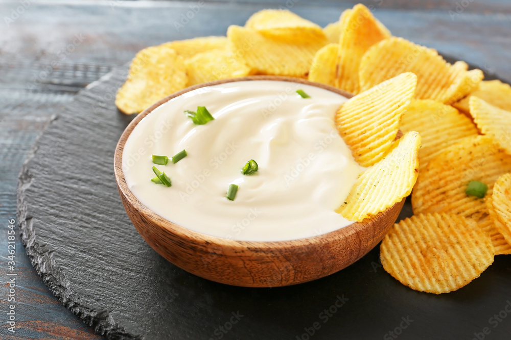 Bowl with tasty sour cream and potato chips on table