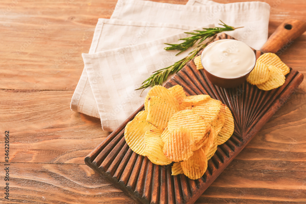 Board with tasty sour cream and potato chips on table