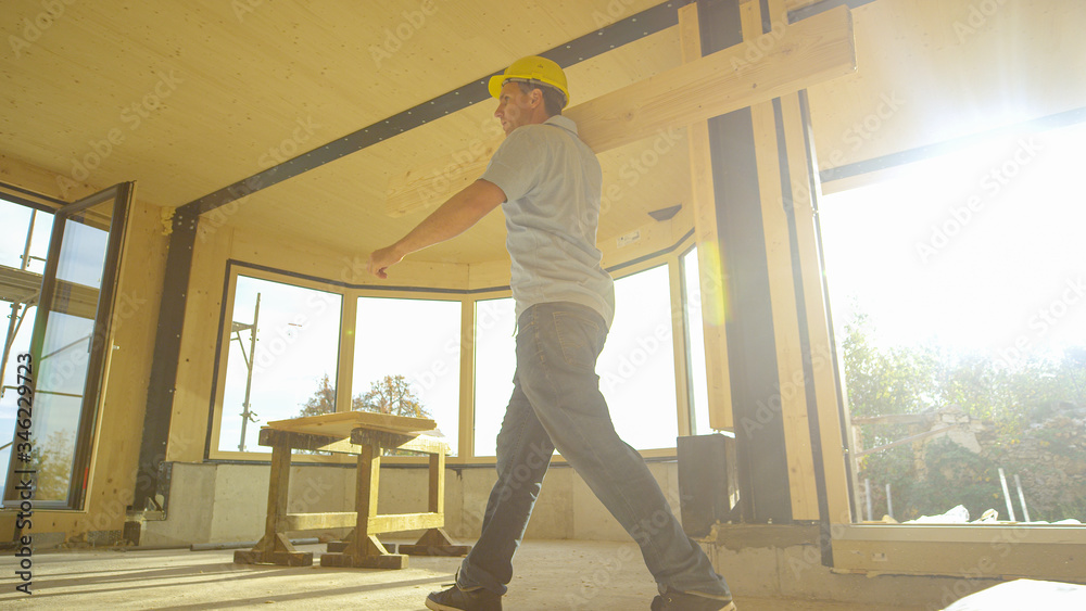 LOW ANGLE: Construction site supervisor carries a log across prefabricated house