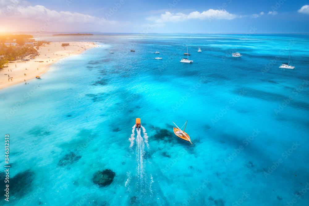 Aerial view of the yachts, fishing boats on tropical sea coast with sandy beach at sunset. Summer tr