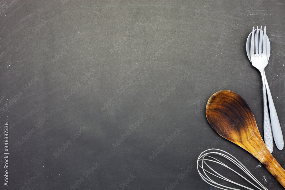 Stainless steel spoon and fork on black wood or chalkboard background.