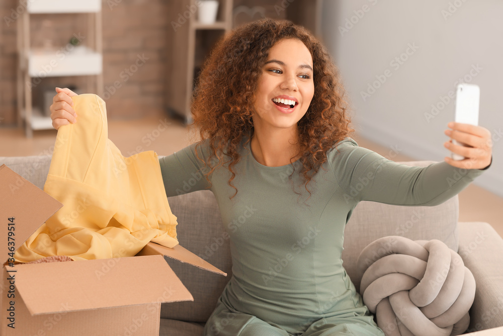 Young woman with received new clothes taking photo at home