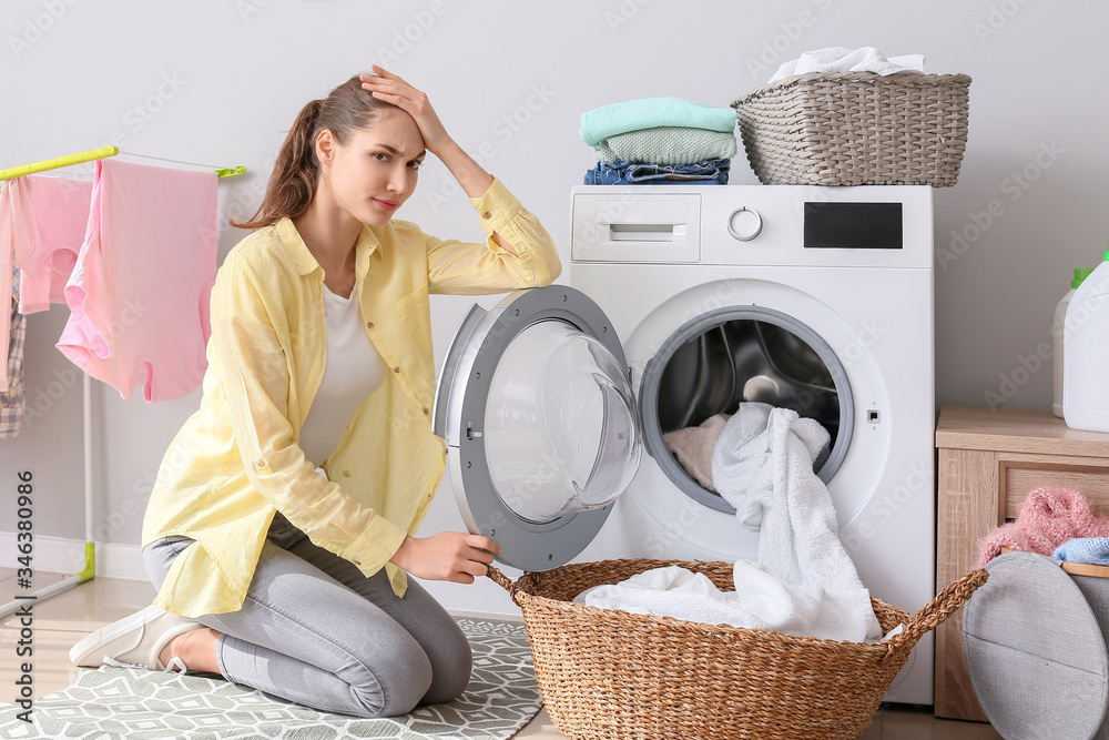 Tired young woman doing laundry in bathroom