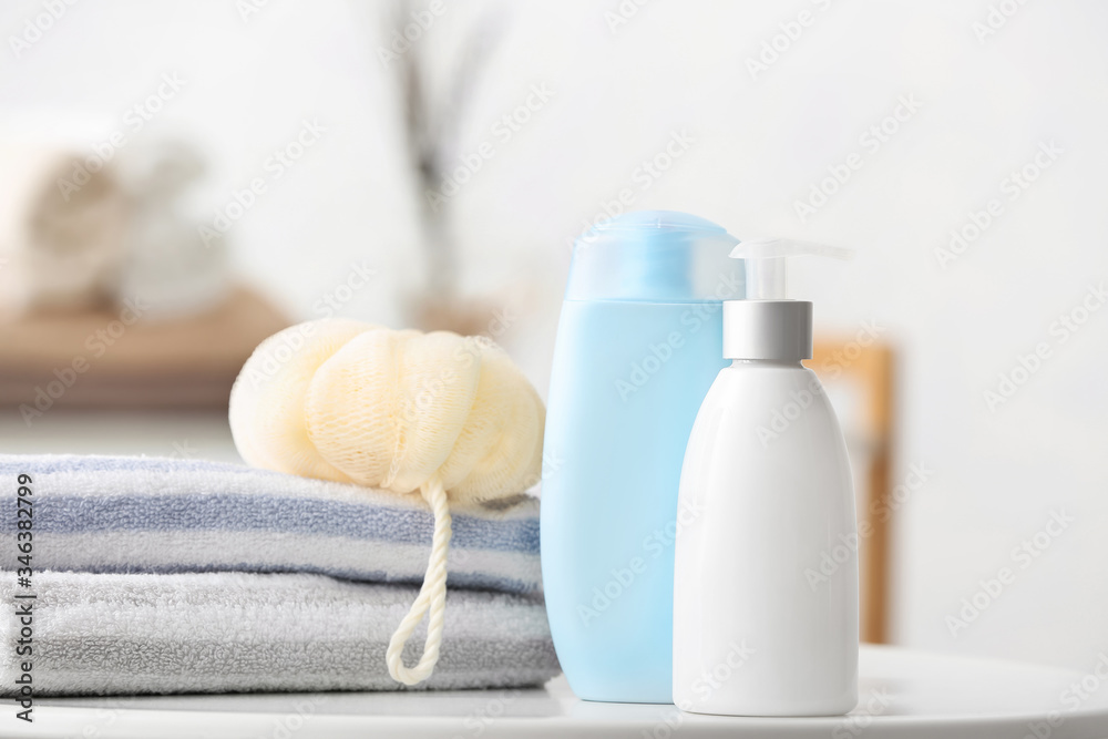 Different shower gels, towel and loofah on table in bathroom