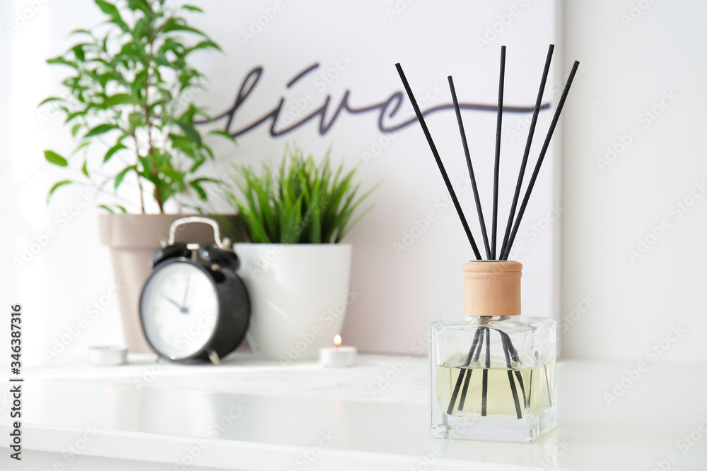 Reed diffuser, clock and houseplants on table in room