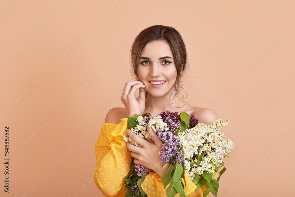 Beautiful young woman with lilac flowers on color background