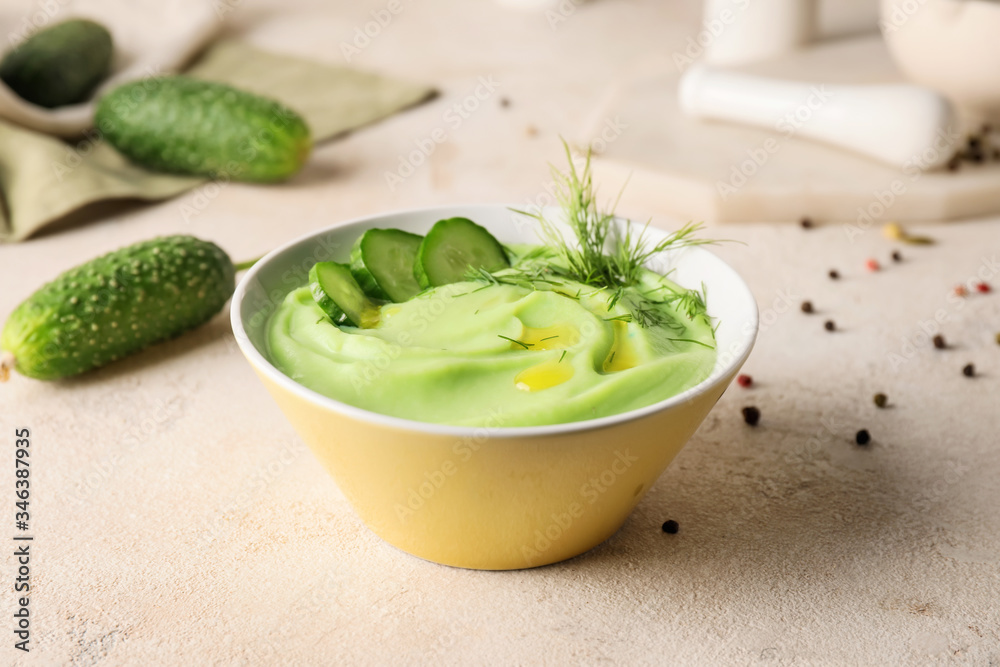 Bowl with cold cucumber soup on light background