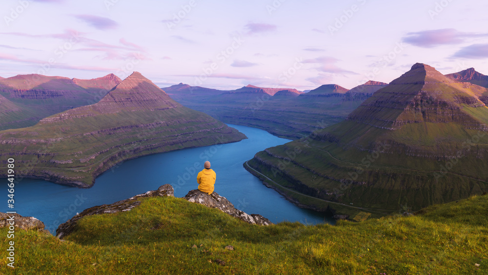 Lonely tourist in yellow jacket looking over majestic fjords of Funningur, Eysturoy island, Faroe Is