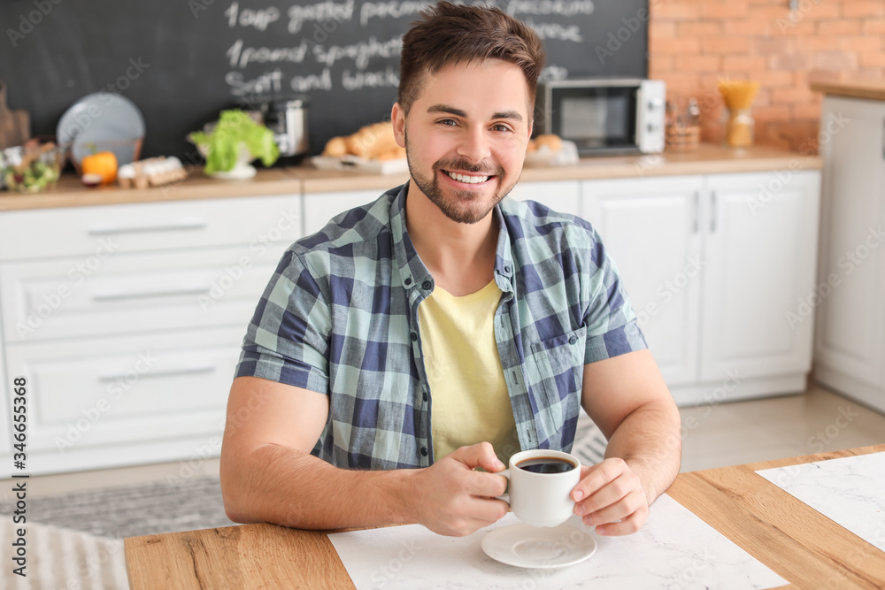 Young man drinking hot coffee in kitchen