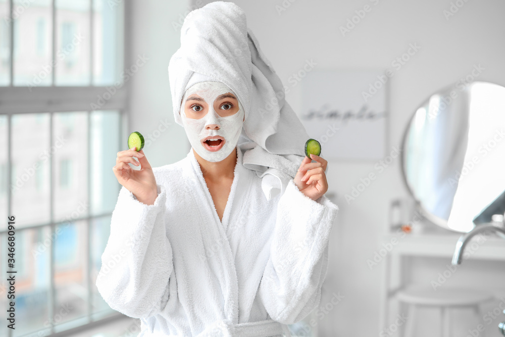 Beautiful young African-American woman with cucumber slices and facial mask in bathroom