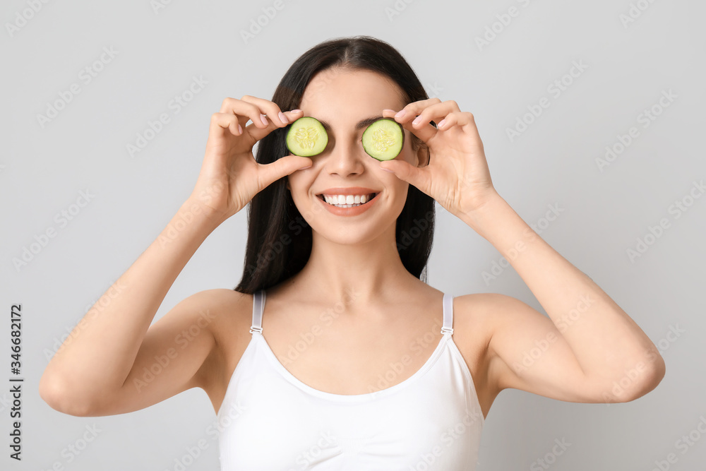 Beautiful young woman with cucumber slices on light background