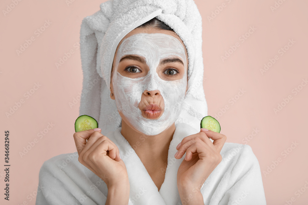 Beautiful young woman with cucumber slices and facial mask on color background