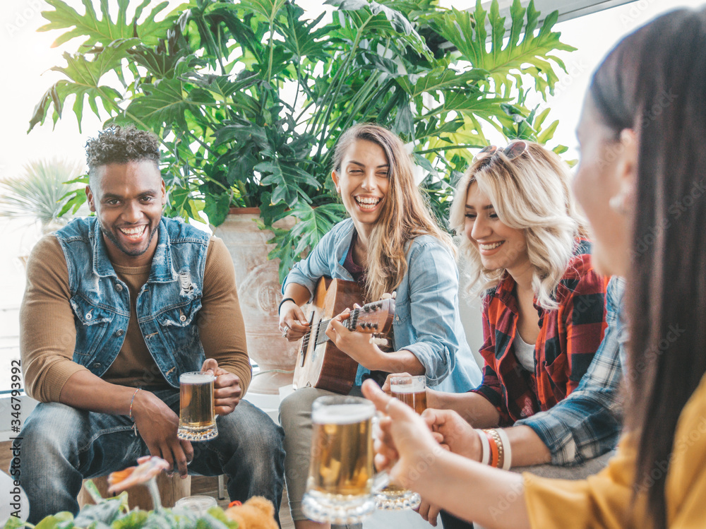 Young multicultural people having fun playing guitar and drinking beer all together at holiday. Frie