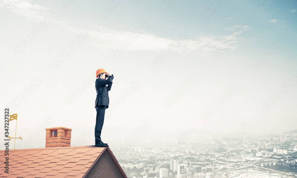 Engineer man standing on roof and looking in binoculars. Mixed m